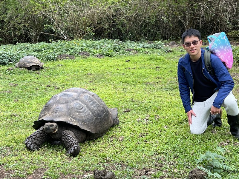 Xiangyi Huang kneeling on grass near a giant tortoise.